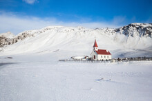 Small Church With Bright Red Roof Stands In Contrast To Snow Covered Field And Mountains In Iceland