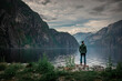Man standing at waterfront of lake in the mountain landscape Eidfjord in Norway, looking into the fjord, clouds in the sky