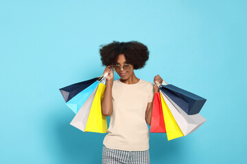 Wall Mural - Happy African American woman in sunglasses with shopping bags on light blue background