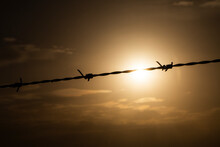 A Barbed Wire Fence Silhouetted By A Sunset