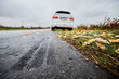Close up of car brake path on edge of asphalt road on the background of parked white car, fallen yellow leaves on the grass and gray sky. Emergency braking tracks on edge of highway.
