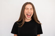 Portrait of excited young woman screaming or shouting over white background. Caucasian lady wearing black T-shirt posing with closed eyes and open mouth. Excitement and happiness concept