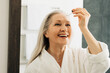 © Artem Varnitsin - Smiling senior woman holding pipette with hyaluronic acid. Happy female applying liquid facial treatment.