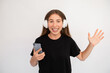 © KAMPUS - Portrait of happy young woman in headphones holding smartphone. Caucasian lady wearing black T-shirt listening to mobile mp3 player over white background. Music and mobile app concept