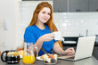 Smart corpulent female student learning at computer in the morning at breakfast