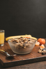 Granola cereal oatmeal with chocolate, banana and nuts in a bowl on dark wooden board