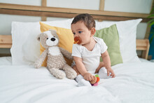 Adorable Hispanic Baby Sucking Pacifier Sitting On Bed At Bedroom