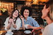 © Jose Calsina - A group of young women talking and laughing sitting on a coffee shop or restaurant. Two ladies smiling and looking his friend holding a cup. Three girls having fun cahtting on a bar. Lifestyle concept