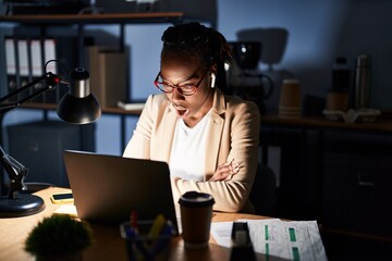 Wall Mural - Beautiful black woman working at the office at night afraid and shocked with surprise expression, fear and excited face.