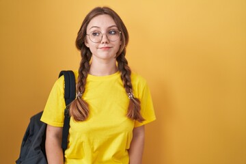 Wall Mural - Young caucasian woman wearing student backpack over yellow background smiling looking to the side and staring away thinking.