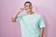 © Krakenimages.com - Handsome hispanic man standing over pink background doing peace symbol with fingers over face, smiling cheerful showing victory