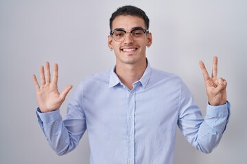 Canvas Print - Handsome hispanic man wearing business clothes and glasses showing and pointing up with fingers number seven while smiling confident and happy.