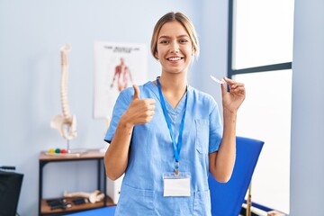 Canvas Print - Young blonde woman holding plastic aligner for bruxism smiling happy and positive, thumb up doing excellent and approval sign