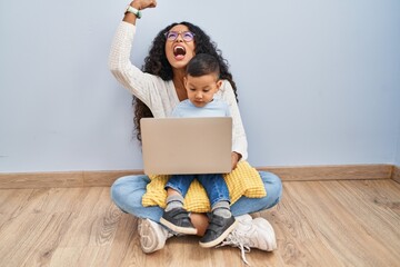 Sticker - Young hispanic mother and kid using computer laptop sitting on the floor angry and mad raising fist frustrated and furious while shouting with anger. rage and aggressive concept.