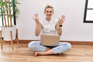 Sticker - Young blonde woman using computer laptop sitting on the floor at the living room showing and pointing up with fingers number nine while smiling confident and happy.