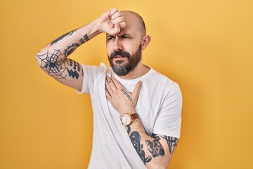 Wall Mural - Young hispanic man with tattoos standing over yellow background touching forehead for illness and fever, flu and cold, virus sick