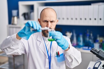 Wall Mural - Young bald man scientist  pouring liquid on test tube at laboratory