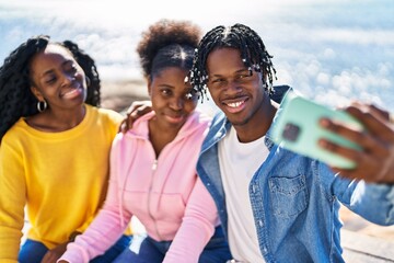 African american friends making selfie by the smartphone sitting on bench at seaside