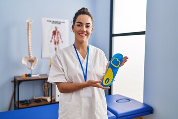 Canvas Print - Young hispanic woman holding shoe insole at physiotherapy clinic smiling with a happy and cool smile on face. showing teeth.