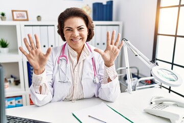 Poster - Middle age hispanic woman wearing doctor uniform and stethoscope at the clinic showing and pointing up with fingers number ten while smiling confident and happy.