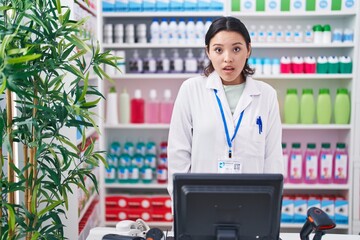 Sticker - Hispanic young woman working at pharmacy drugstore scared and amazed with open mouth for surprise, disbelief face