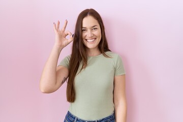 Sticker - Beautiful brunette woman standing over pink background smiling positive doing ok sign with hand and fingers. successful expression.