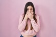 Young brunette woman standing over pink background shocked covering mouth with hands for mistake. secret concept.