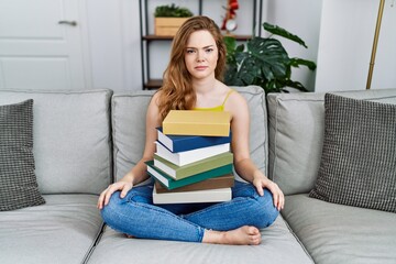 Sticker - Young caucasian woman sitting on the sofa with books at home skeptic and nervous, frowning upset because of problem. negative person.