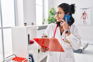 Sticker - Young latin woman doctor talking on smartphone reading document at clinic