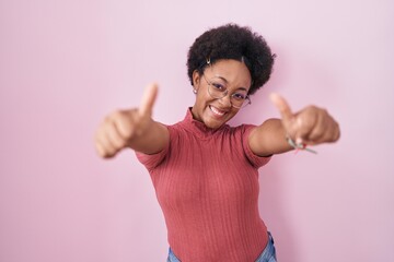 Sticker - Beautiful african woman with curly hair standing over pink background approving doing positive gesture with hand, thumbs up smiling and happy for success. winner gesture.