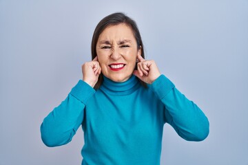 Canvas Print - Middle age hispanic woman standing over isolated background covering ears with fingers with annoyed expression for the noise of loud music. deaf concept.