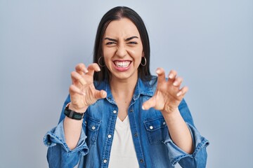 Wall Mural - Hispanic woman standing over blue background smiling funny doing claw gesture as cat, aggressive and sexy expression