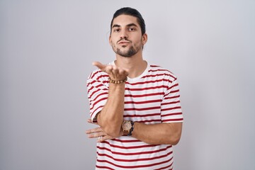 Wall Mural - Hispanic man with long hair standing over isolated background looking at the camera blowing a kiss with hand on air being lovely and sexy. love expression.