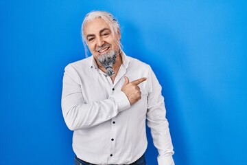 Wall Mural - Middle age man with grey hair standing over blue background cheerful with a smile on face pointing with hand and finger up to the side with happy and natural expression