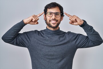 Sticker - Handsome latin man standing over isolated background smiling pointing to head with both hands finger, great idea or thought, good memory