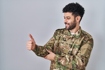 Poster - Arab man wearing camouflage army uniform looking proud, smiling doing thumbs up gesture to the side