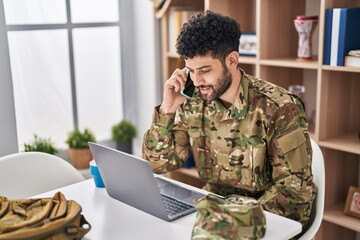 Wall Mural - Young arab man army soldier using laptop talking on the smartphone at home