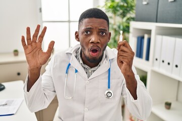 Poster - African american doctor man holding eye drops scared and amazed with open mouth for surprise, disbelief face