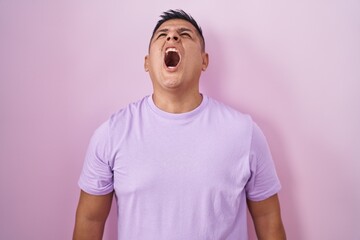 Sticker - Young hispanic man standing over pink background angry and mad screaming frustrated and furious, shouting with anger. rage and aggressive concept.