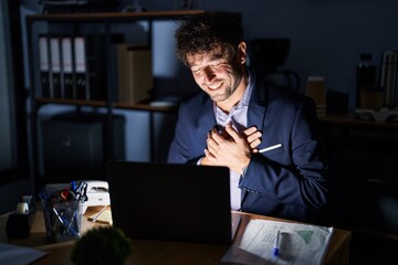 Canvas Print - Hispanic young man working at the office at night smiling with hands on chest with closed eyes and grateful gesture on face. health concept.