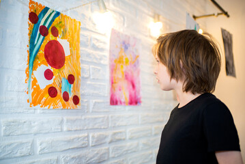 a small child, a student of an art school, studies paintings at an exhibition in a gallery