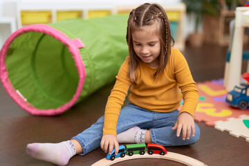 Poster - Adorable hispanic girl playing with cars toy sitting on floor at kindergarten