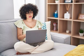 Canvas Print - Young brunette woman with curly hair using laptop sitting on the sofa at home depressed and worry for distress, crying angry and afraid. sad expression.