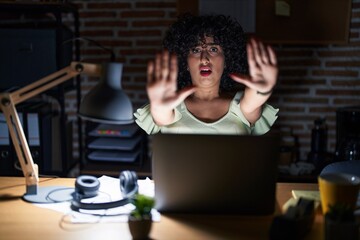 Poster - Young brunette woman with curly hair working at the office at night doing stop gesture with hands palms, angry and frustration expression