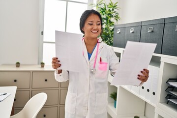 Wall Mural - Young chinese woman wearing doctor uniform reading document at clinic