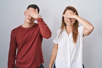 Canvas Print - Mother and son standing together over isolated background covering eyes with hand, looking serious and sad. sightless, hiding and rejection concept