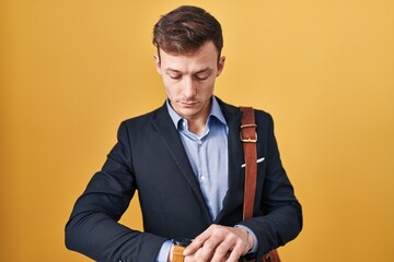 Caucasian business man over yellow background checking the time on wrist watch, relaxed and confident