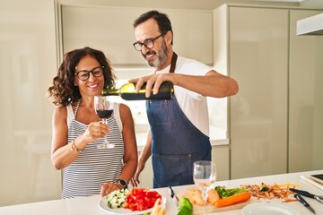 Wall Mural - Middle age hispanic couple cooking and pouring wine on glass at kitchen