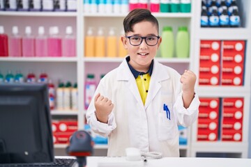 Wall Mural - Young hispanic kid working at pharmacy drugstore celebrating surprised and amazed for success with arms raised and eyes closed