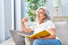 Middle Age Woman Reading Book Sitting On Sofa At Home